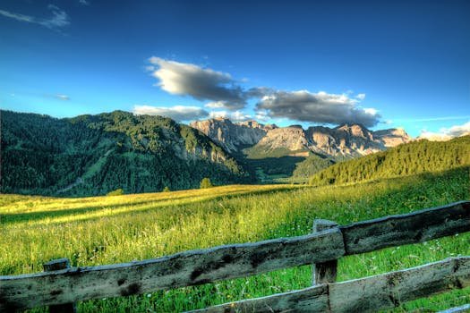 An idyllic mountain landscape with a wooden fence under a clear blue sky.