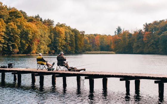 Two men fishing on a pier surrounded by autumn foliage at a scenic lake.
