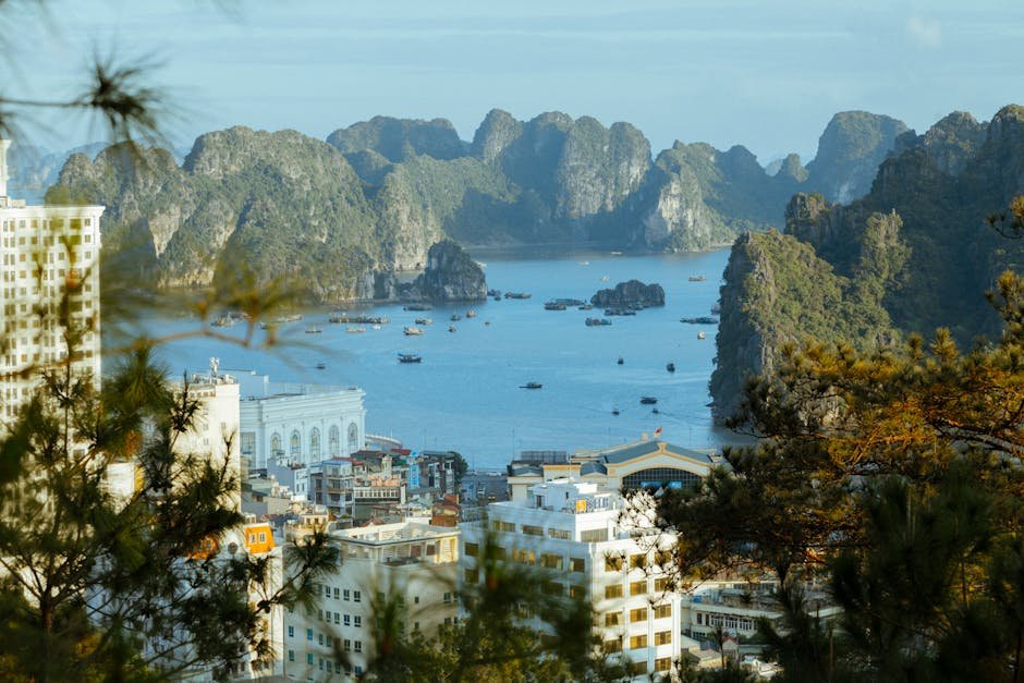 Aerial view of Halong Bay with city and rock formations under a clear sky.